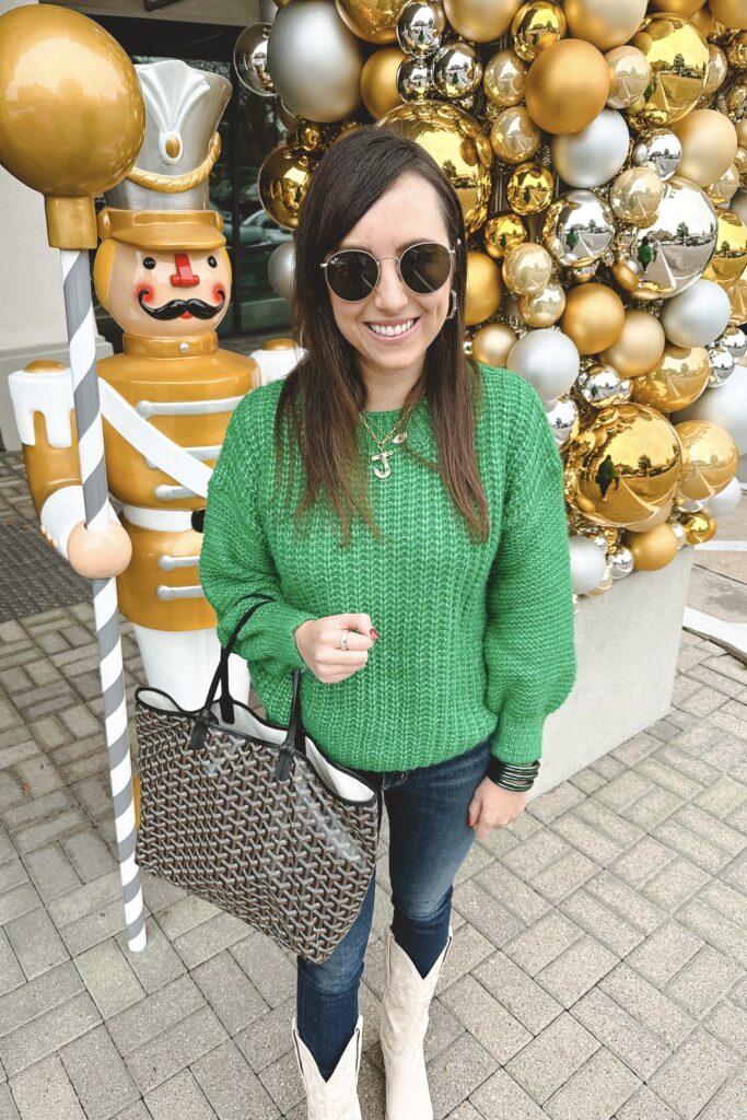 green sweater with goyard tote and white cowgirl boots